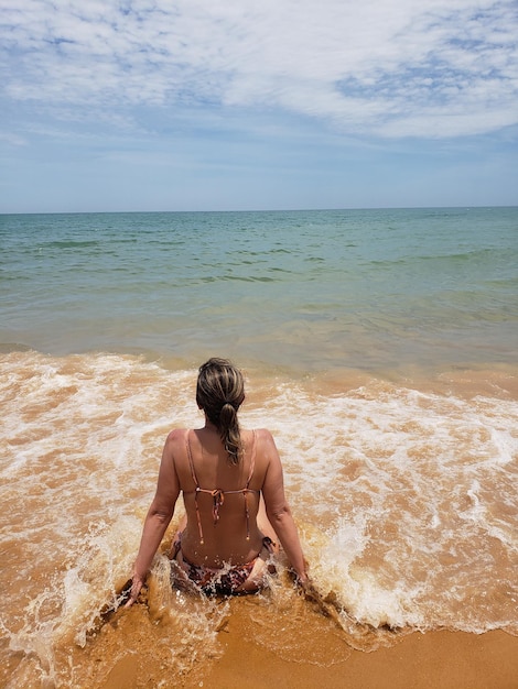 Foto vista posteriore di una donna seduta sulla spiaggia contro il cielo