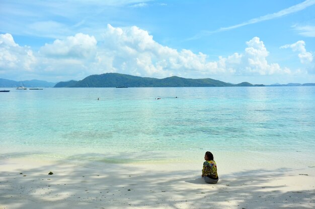 Rear view of woman sitting at beach against sky