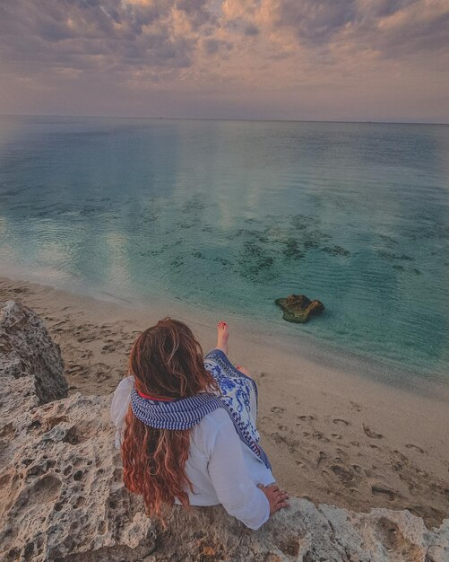 Foto vista posteriore di una donna seduta sulla spiaggia durante il tramonto