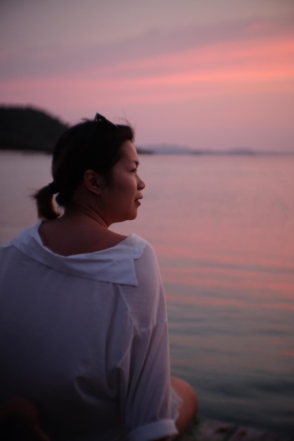Foto vista posteriore di una donna seduta sulla spiaggia durante il tramonto