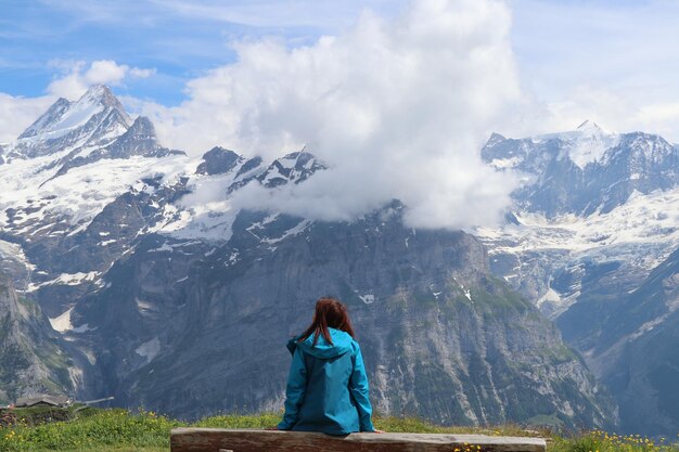 Rear view of woman sitting on bench against mountain range