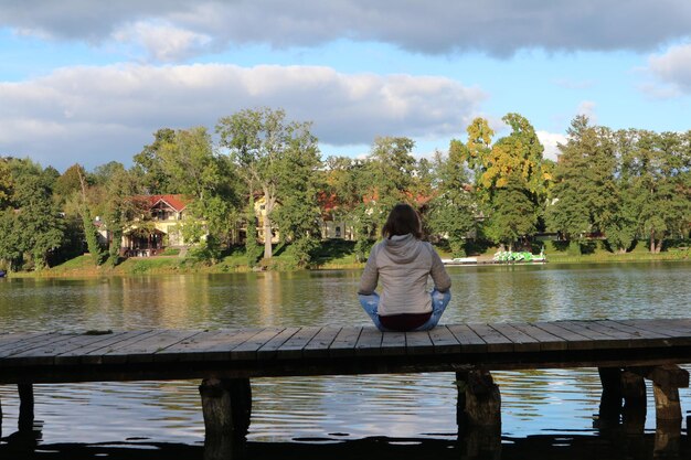 Photo rear view of woman sitting by lake against sky