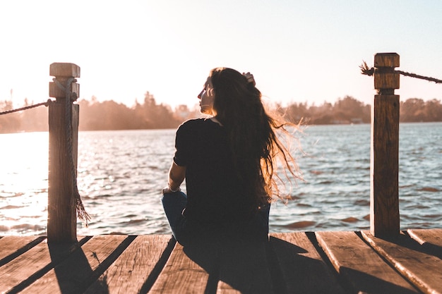 Foto vista posteriore di una donna seduta sul lago sul molo