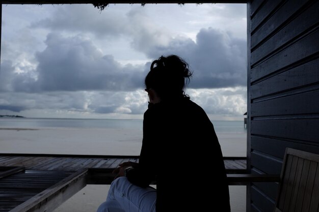 Foto vista posteriore di una donna seduta su una sedia sulla spiaggia contro il cielo