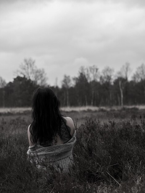 Foto vista posteriore di una donna seduta sul campo contro il cielo