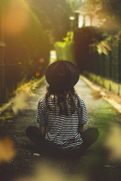 Foto vista posteriore di una donna seduta sul sentiero durante una giornata di sole