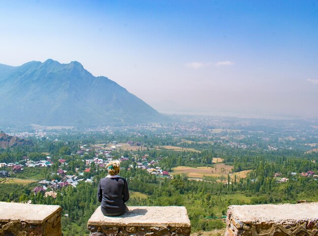 明るい空を背景に山の上に座っている女性の後ろの景色