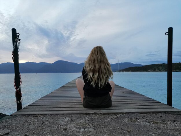 Photo rear view of woman sitting on pier against sky