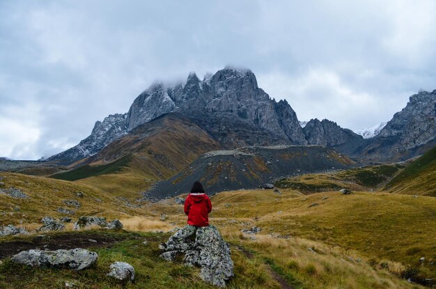 rear view of woman sitting on rock against mountains