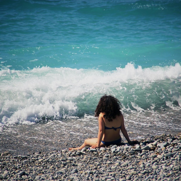 Foto vista posteriore di una donna seduta su una roccia sulla spiaggia