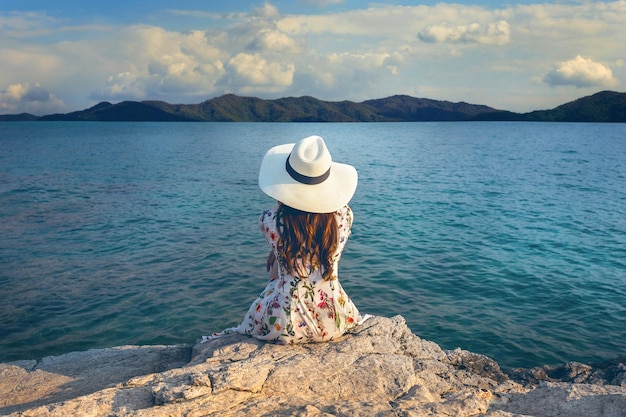 rear view of woman sitting on rock by sea against mountains