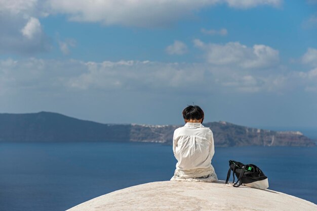 하늘을 배경으로 바다에 바위 위에 앉아있는 여성의 뒷면