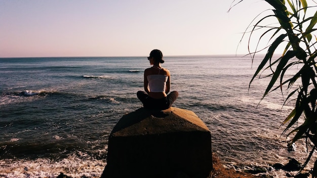 Photo rear view of woman sitting on structure at beach during sunset