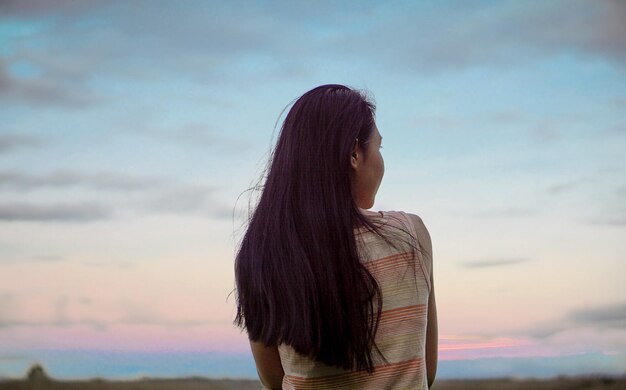 空に向かって海に向かって立っている女性の後ろの景色