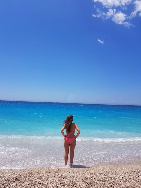 Rear view of woman standing at beach against blue sky