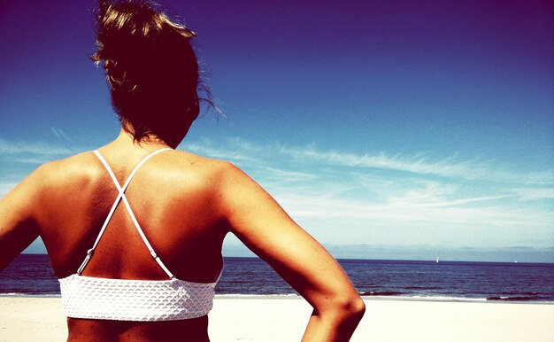 Rear view of woman standing at beach against sky