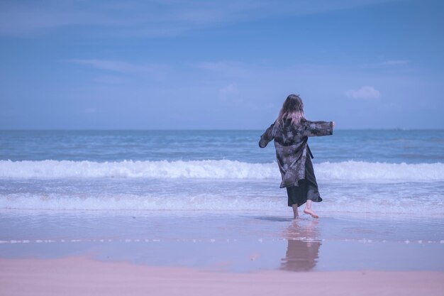 Rear view of woman standing at beach against sky