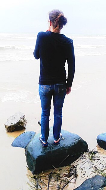 Rear view of woman standing at beach against sky