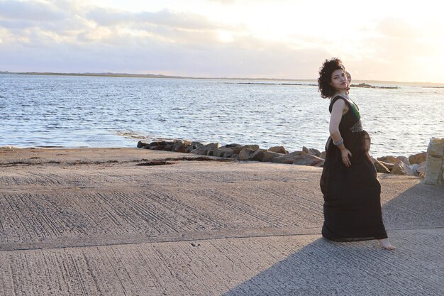 Rear view of woman standing at beach against sky