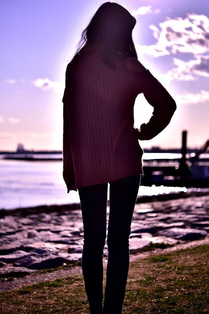 Rear view of woman standing at beach during sunset