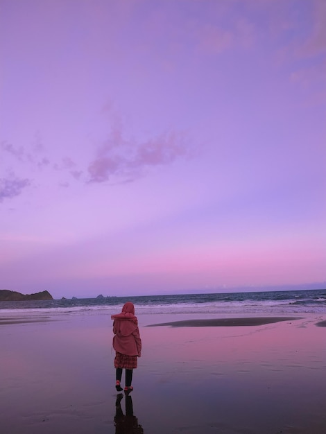 Rear view of woman standing on beach during sunset