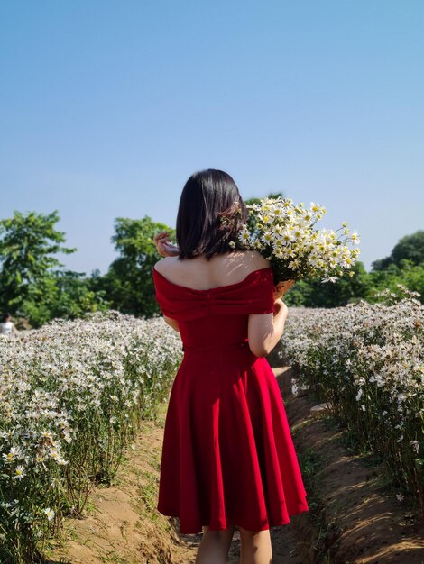 空に向かって花をかせている植物のそばに立っている女性の後ろの景色