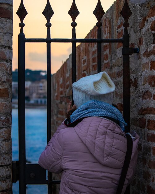 Foto vista posteriore di una donna in piedi vicino al cancello e al muro in inverno