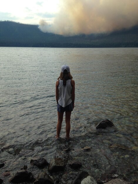 Foto vista posteriore di una donna in piedi vicino al lago contro il cielo