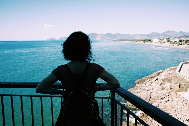 Rear view of woman standing by railing against sea