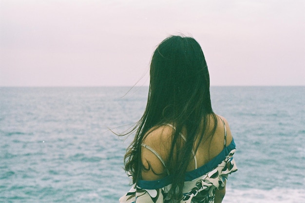 rear view of woman standing by sea against clear sky