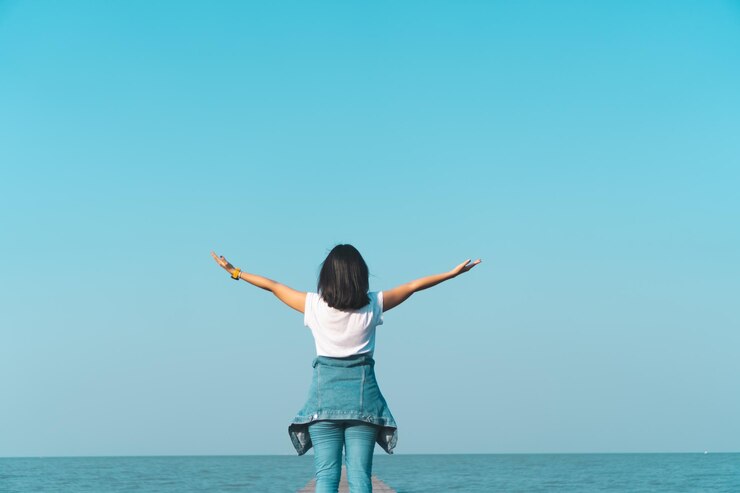 Photo 澄んだ空に照らされて海辺に立っている女性の後ろの景色