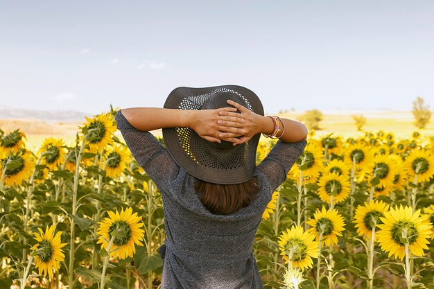 Foto vista posteriore di una donna in piedi vicino alle piante di girasole contro il cielo