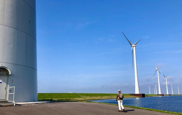 Rear view of woman standing by windmills against blue sky