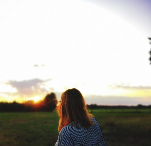 夕暮れの空に向かって畑に立っている女性の後ろの景色