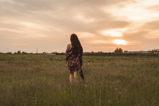 Rear view of woman standing on field against sky during sunset