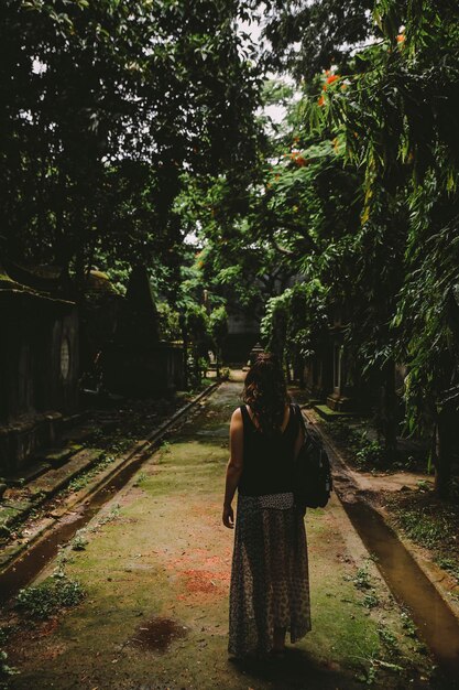 Foto vista posteriore di una donna in piedi sul sentiero tra gli alberi