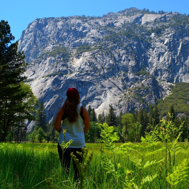 Foto vista posteriore di una donna in piedi su un campo erboso in mezzo alla montagna