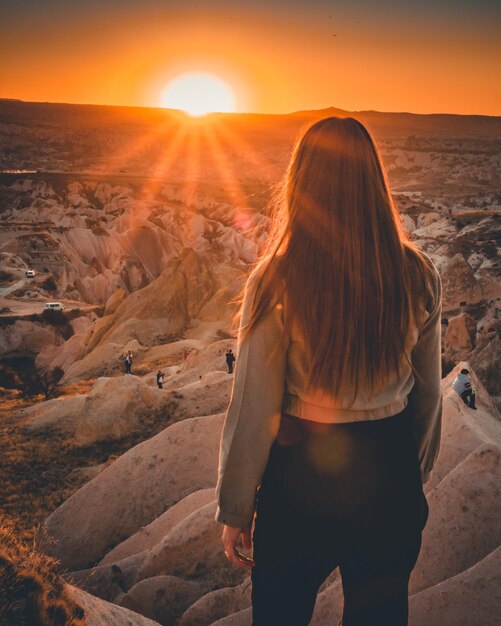 夕暮れの空に向かって地面に立っている女性の後ろの景色
