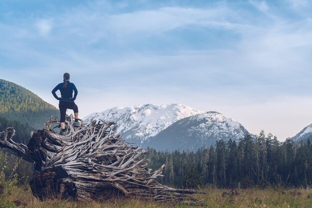 Foto vista posteriore di una donna in piedi su un tronco nella foresta contro un cielo nuvoloso