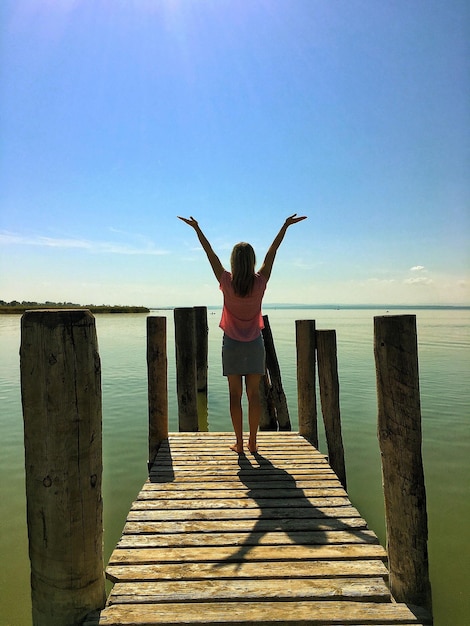 Foto vista posteriore di una donna in piedi sul molo contro il mare