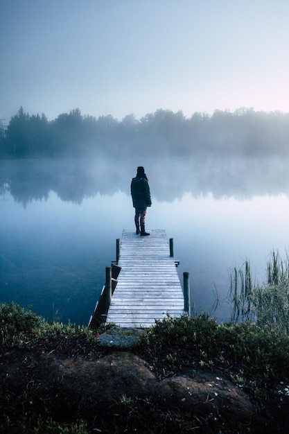 Foto vista posteriore di una donna in piedi sul molo sopra il lago contro il cielo