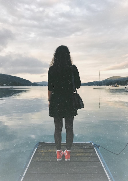 Rear view of woman standing on pier over sea against sky