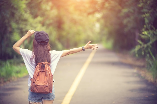 樹木に背を向けて道路に立っている女性の後ろの景色