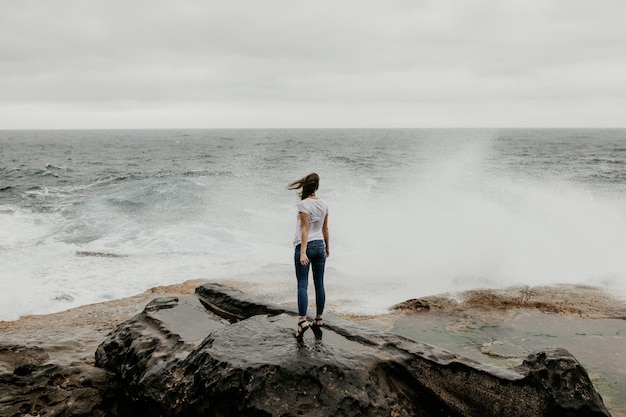 Photo rear view of woman standing on rock at beach