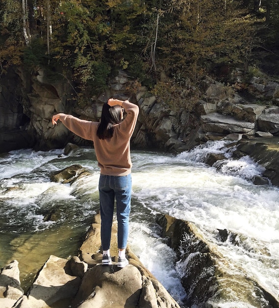 Rear view of woman standing on rock by river