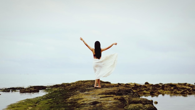 Photo rear view of woman standing on rock by sea against sky