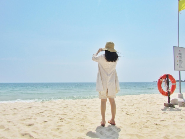 은 하늘 을 배경 으로 해변 의 모래 위 에 서 있는 여자 의 뒷면
