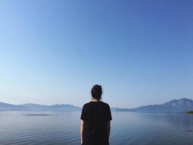 rear view of woman standing in sea against clear sky