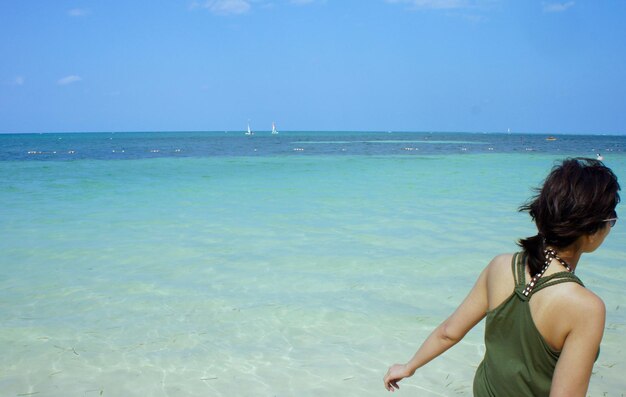 Rear view of woman standing at sea shore against blue sky