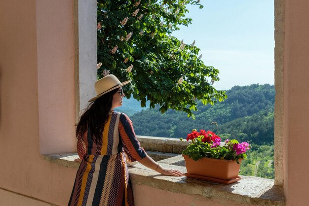 Photo rear view of woman standing on terrace of old building looking at beautiful landscape in summer